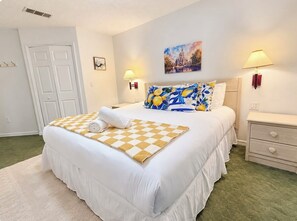 A hotel room with a large bed, a bedside table, a nightstand, a wall-mounted lamp, and a door. - 20 Min to Disney World | 4BR Pool Home (Kissimmee)