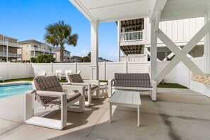 An outdoor patio with white furniture, a pool, and a view of a residential area. - This Must Be The Place (Ocean Isle Beach)