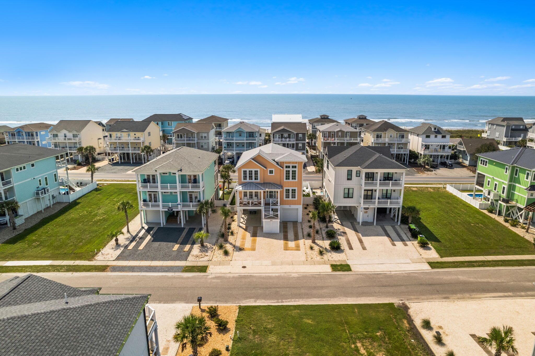 A coastal residential area with multi-story houses featuring balconies, a clear sky, and a view of the ocean.