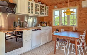 A modern kitchen with white cabinetry, a built-in dishwasher, and a dining area with a wooden table and chairs. - Gorgeous home in Roslev with house a panoramic view (Roslev)