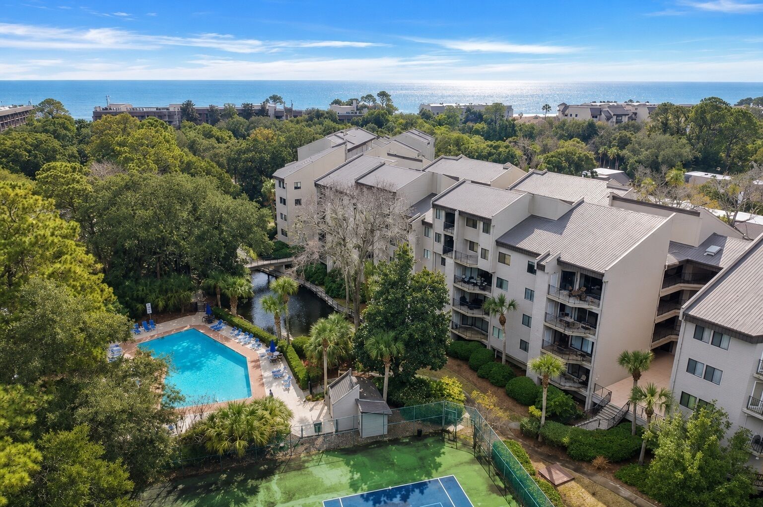 Ein mehrstöckiges Hotel mit Schwimmbad, umgeben von üppiger Vegetation, einem Tennisplatz und Blick auf den Ozean.