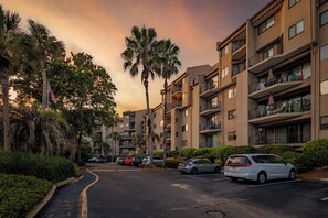 Edifício residencial com vários andares, varandas, área de estacionamento e palmeiras.