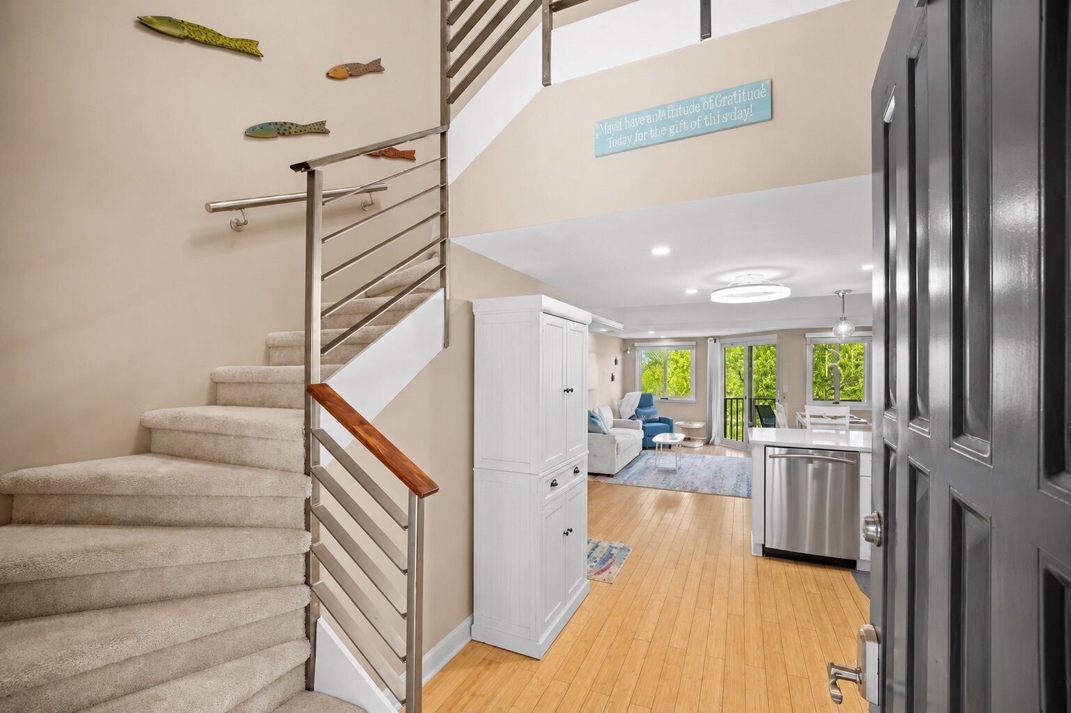 Una escalera con barandilla, una zona de cocina con mesa y sillas, y una sala de estar con sofá y sillón.