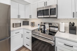 A modern kitchen with stainless steel appliances, white cabinetry, and a marble countertop.