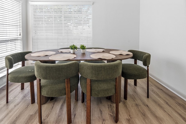 A round dining table with six chairs, a small potted plant, and woven placemats.