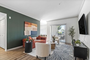 A modern living room with a sofa, armchair, and a flat-screen TV mounted on the wall.