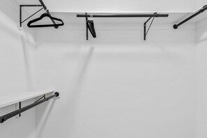 A white wall with a metal rack holding a coat and a towel, and a metal shelf with a towel.