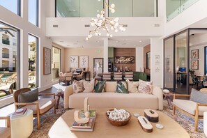 A spacious lobby with a high ceiling, a central seating area with a sofa and chairs, a dining area, and a kitchen in the background.