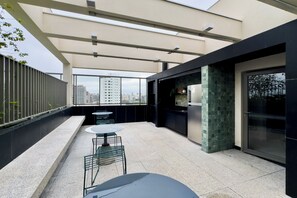 A rooftop terrace with a dining area, a kitchen, and a view of the city skyline. - 1003A - Studio apartment with rooftop pool, 5 minutes from CGH airport. (São Paulo)
