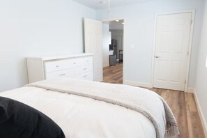 A bedroom with a bed, a dresser, and a door leading to a hallway.
