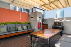 An outdoor patio with a wooden table, a barbecue grill, a sofa with cushions, and a red cabinet. - Suite ejecutiva Piscina y Gym San Isidro (San Isidro)