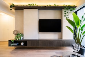 A modern living room with a flat-screen TV mounted on a wall, a dark wood entertainment unit below, and a large potted plant to the right. - Suite ejecutiva Piscina y Gym San Isidro (San Isidro)