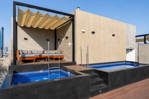 Ein Poolbereich auf dem Dach mit einer Couch und einem Sonnensegel, umgeben von einem modernen Gebäude mit einer strukturierten Wand.