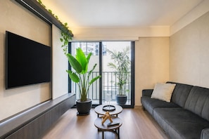 Un salon moderne doté d’un téléviseur à écran plat, d’un canapé foncé, de deux tables rondes ornées d’objets décoratifs et de plantes en pot.