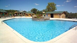 A rectangular swimming pool with a stone border, surrounded by lounge chairs and a wooden building with a green roof.