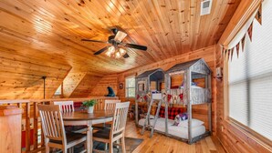 A cozy cabin interior with a dining area, a ceiling fan, and a children's playhouse.
