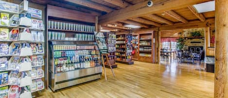 A wooden interior with a glass display case filled with bottled beverages, a wooden ceiling with exposed beams, and a stone fireplace.
