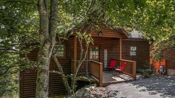 A wooden cabin with a porch, a welcome sign, and a red chair.