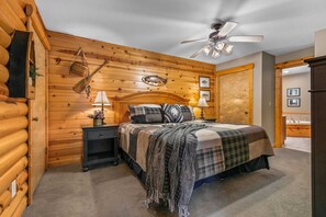 Une chambre de style chalet, avec un lit, deux tables de chevet, un ventilateur de plafond et des murs en bois.