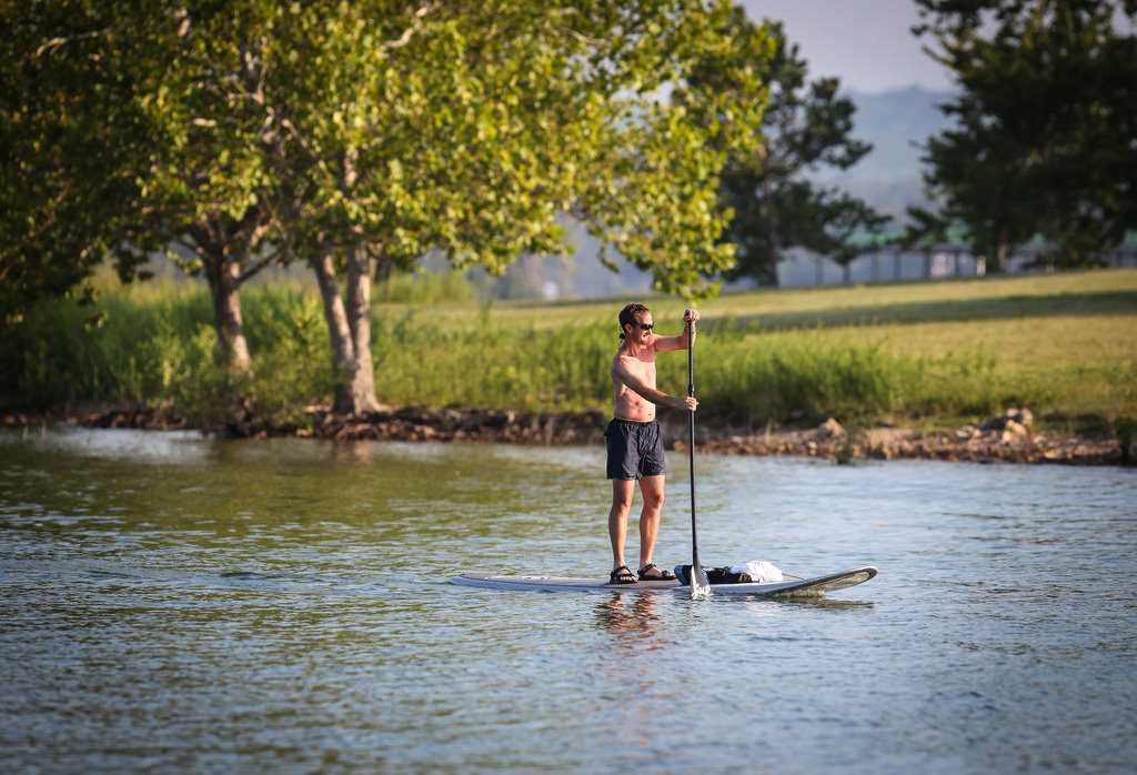 A person paddleboarding on a calm river with trees in the background.