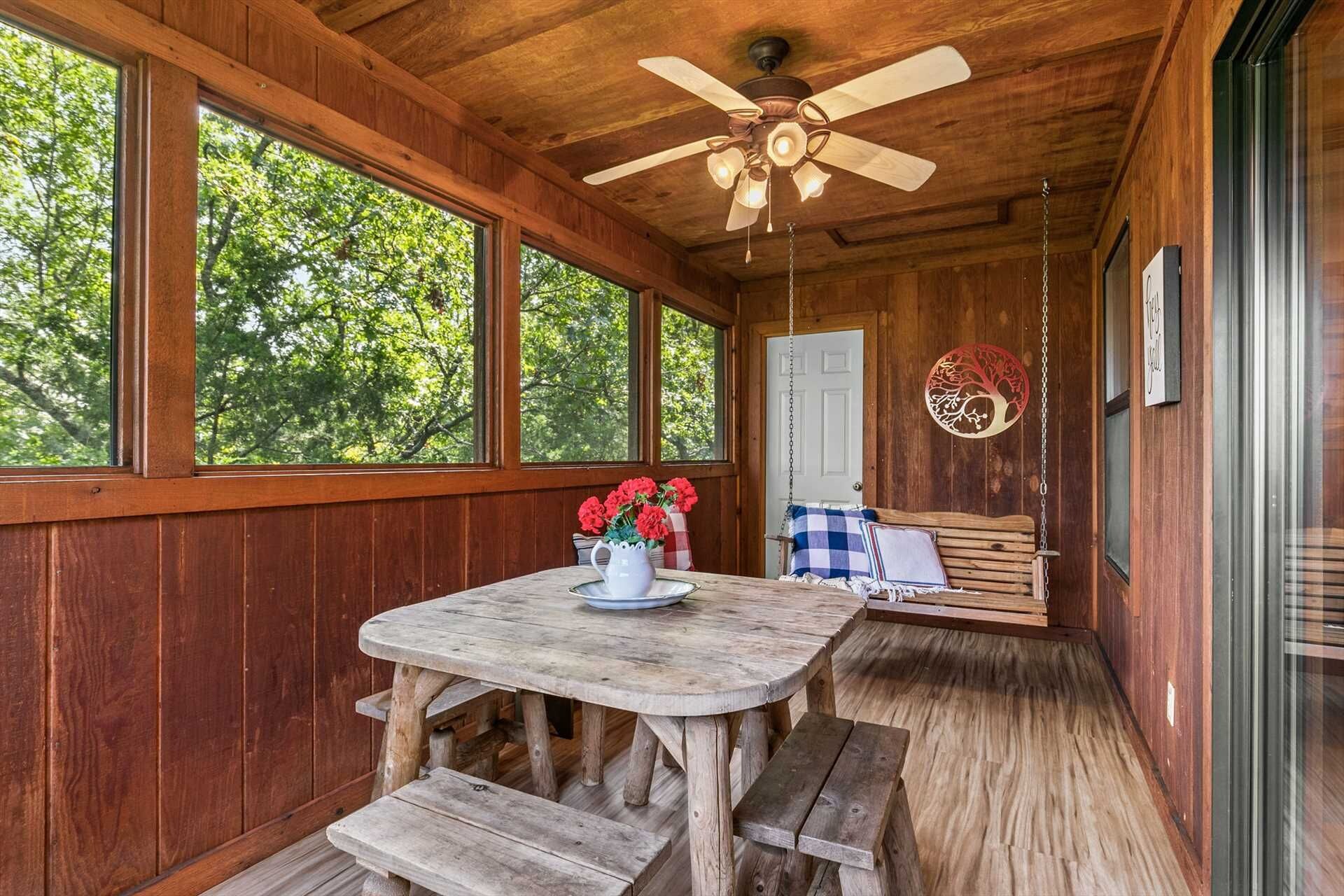 A wooden cabin with a round wooden table and benches, a ceiling fan, and a hanging swing chair.