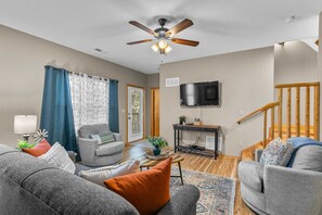 A living room with a ceiling fan, a television mounted on the wall, and a staircase leading to another level. - Incredible 3 Level Luxury Cabin! 4 Bedroom Suites, 2 Living Areas, 3 Pools-21 (Branson)