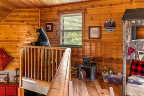 Ein gemütliches Blockhaus-Interieur mit Holzvertäfelung, einem Fenster mit Jalousien, einem Bücherregal und einer Bär-Dekoration.