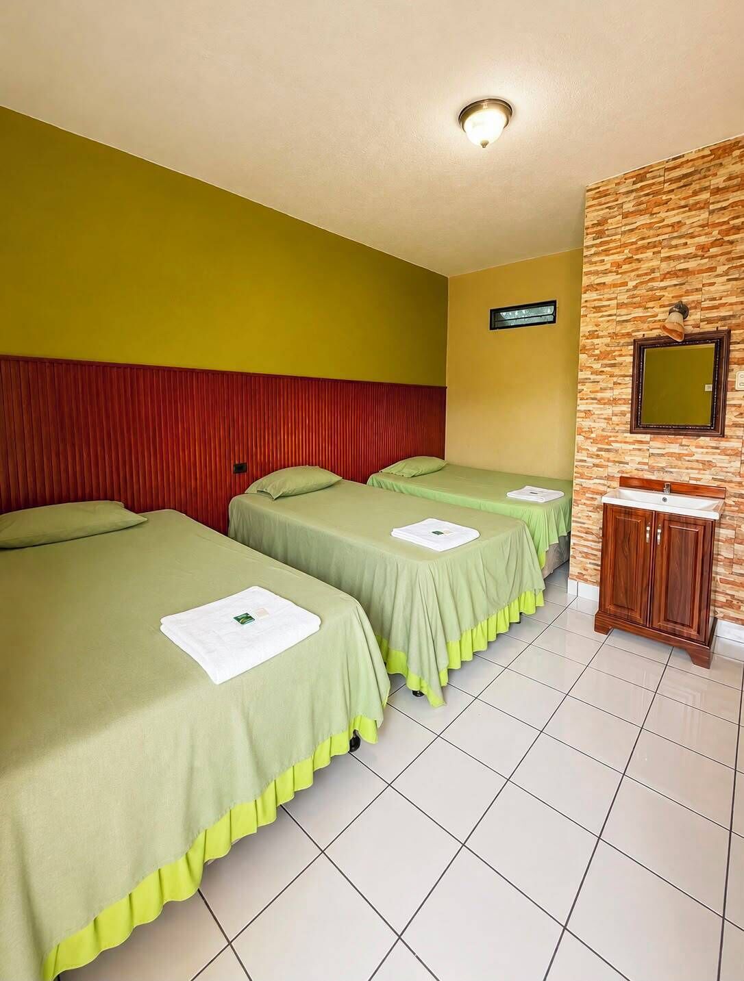 A hotel room with two single beds, a red headboard, a mirror, and a wooden cabinet.