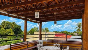 Un patio techado al aire libre con techo de madera, sillas blancas ornamentadas y bancos.