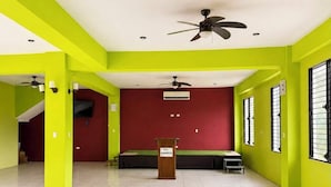 Un vestíbulo de hotel con techo alto, ventiladores de techo, un mostrador de recepción y una escalera que conduce a otro piso.