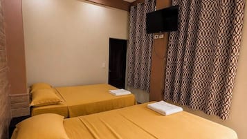 A hotel room with two beds, a ceiling fan, a flat-screen TV, and patterned curtains.