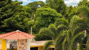 Un patio con un edificio amarillo, una construcción con techo rojo y vegetación circundante.