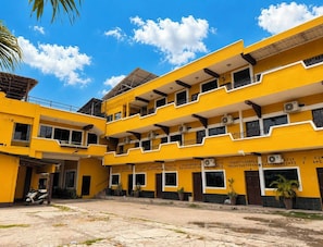 Un edificio amarillo de varios pisos con balcones, aire acondicionado e instalación de plantas.