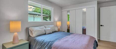 A bedroom with a bed, bedside lamps, a window, and a door.