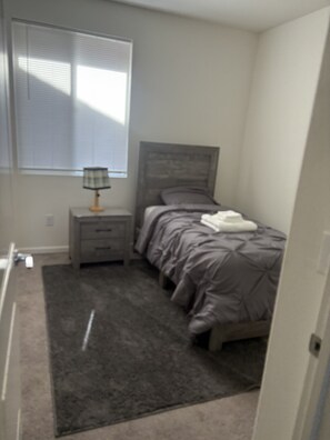 A bedroom with a bed, a nightstand, a lamp, and a window with blinds.