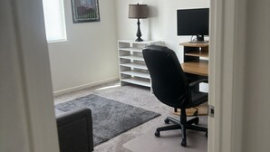 A room with a desk, chair, lamp, and a framed picture on the wall.