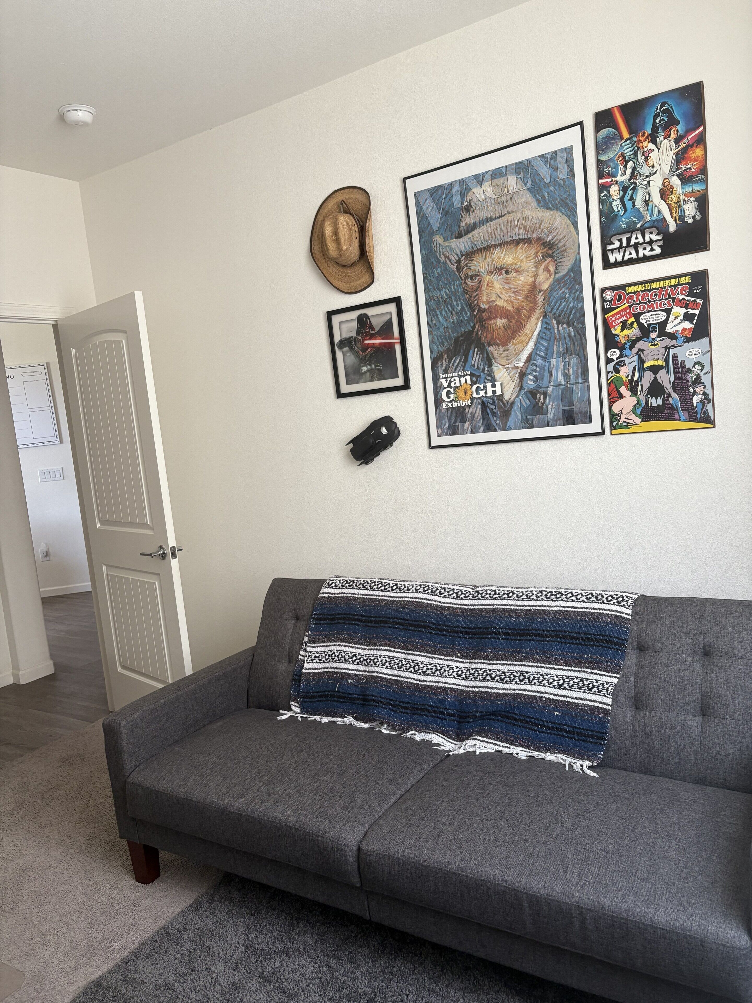 A living room with a grey sofa, a patterned throw blanket, and wall art including a Star Wars poster and a framed picture.