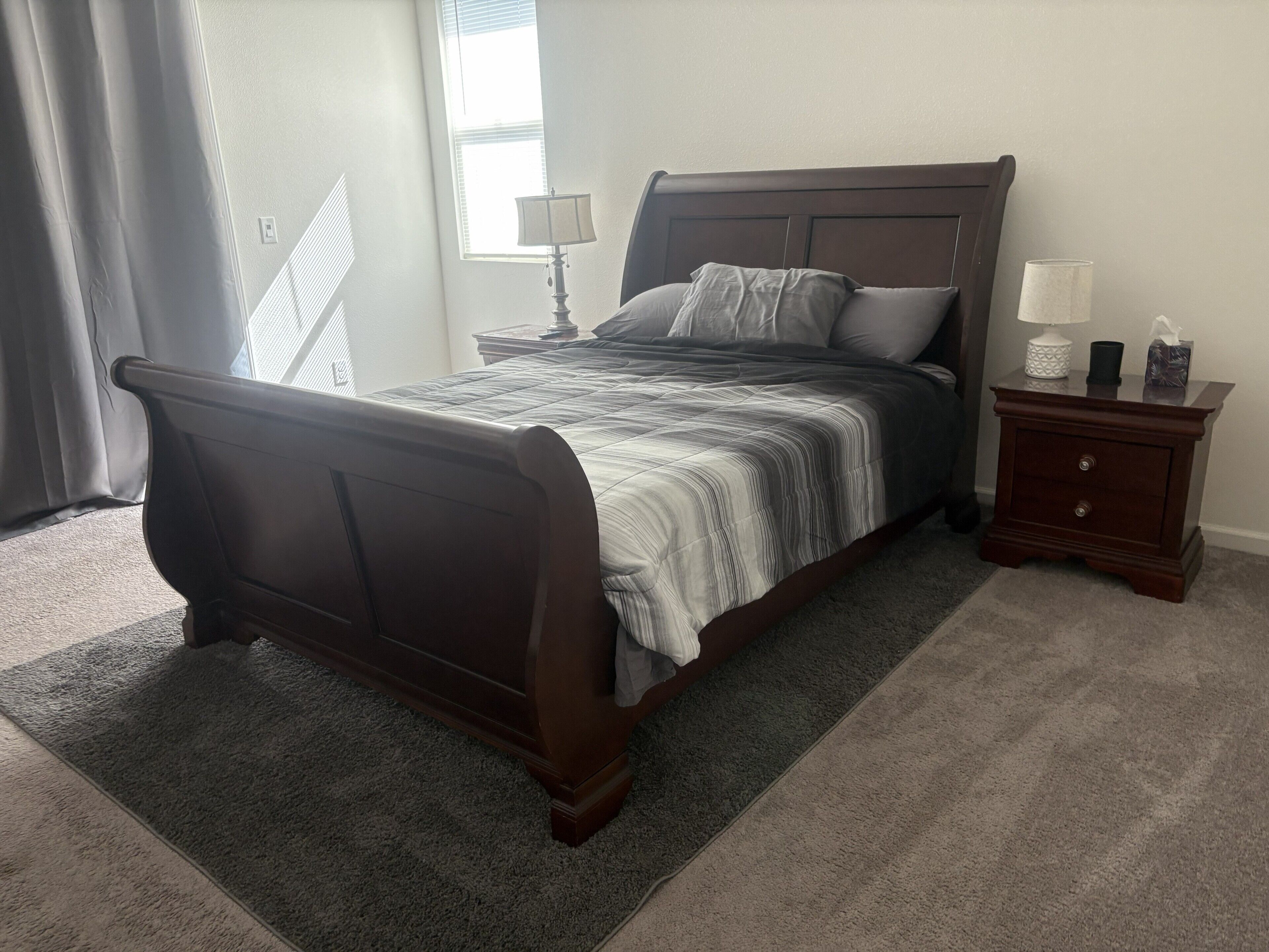 A bedroom with a bed, nightstand, lamp, and a window with curtains.
