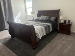 A bedroom with a bed, nightstand, lamp, and a window with curtains. - Beautiful 4-bedroom house with RV parking and pet-friendly. Located in Williams. (Williams)