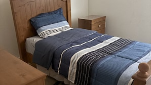 A single bed with a wooden headboard, a nightstand, a drawer, and a framed picture on the wall.