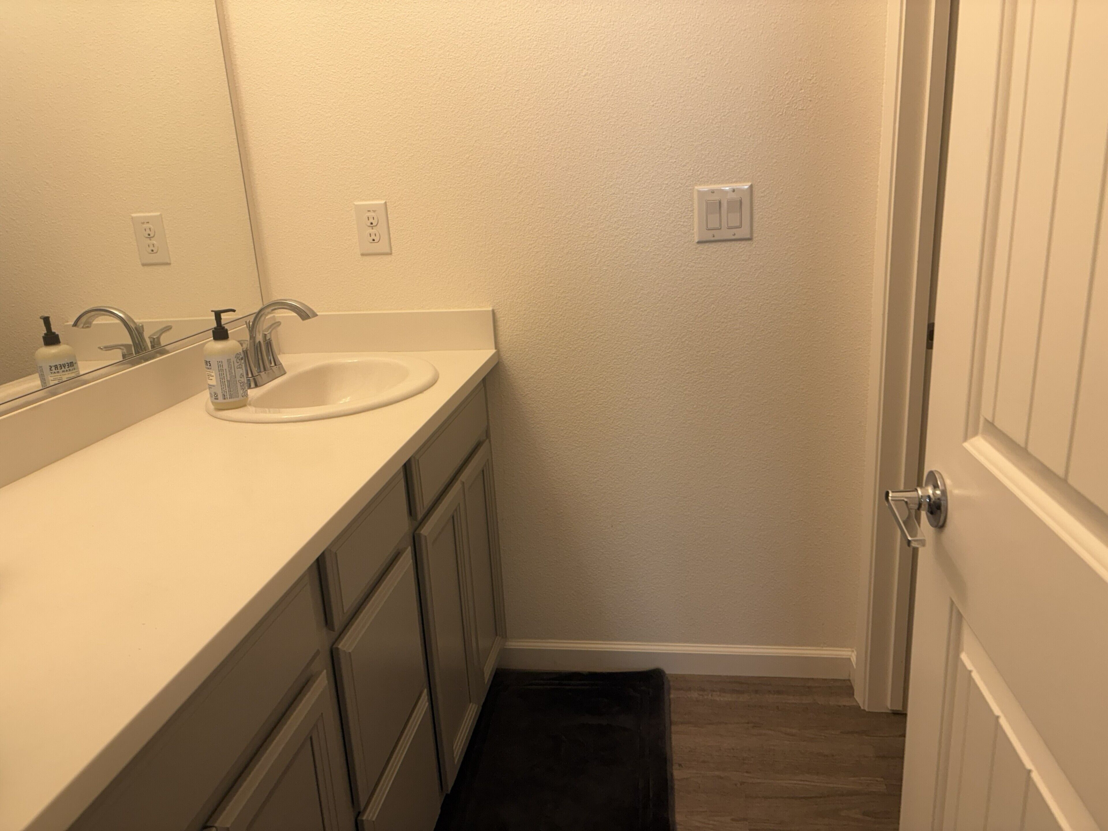 A bathroom with a white sink, a mirror, and a dark-colored towel on the floor.