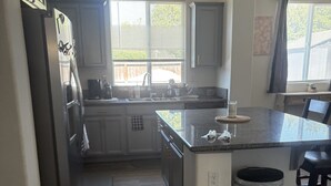 A kitchen with a central island, stainless steel appliances, and a trash can.