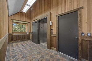 A hallway with a patterned tile floor, wooden walls, and two elevators. - Elk Cove Condo 403 at South Grand Lodge | 2BR + Queen Loft, 3 Baths, Mt. Hood Peek (Government Camp)