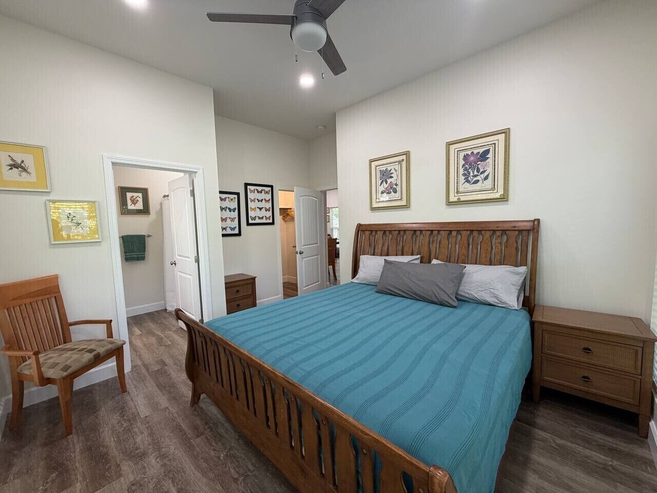 A bedroom with a wooden bed, a nightstand, a chair, and a ceiling fan.