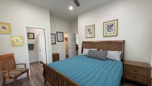 Un dormitorio con cama de madera, mesita de noche, una silla y un ventilador de techo.