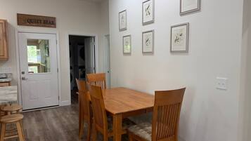 A dining area with a wooden table and chairs, a sign above the door, and framed artwork on the wall.