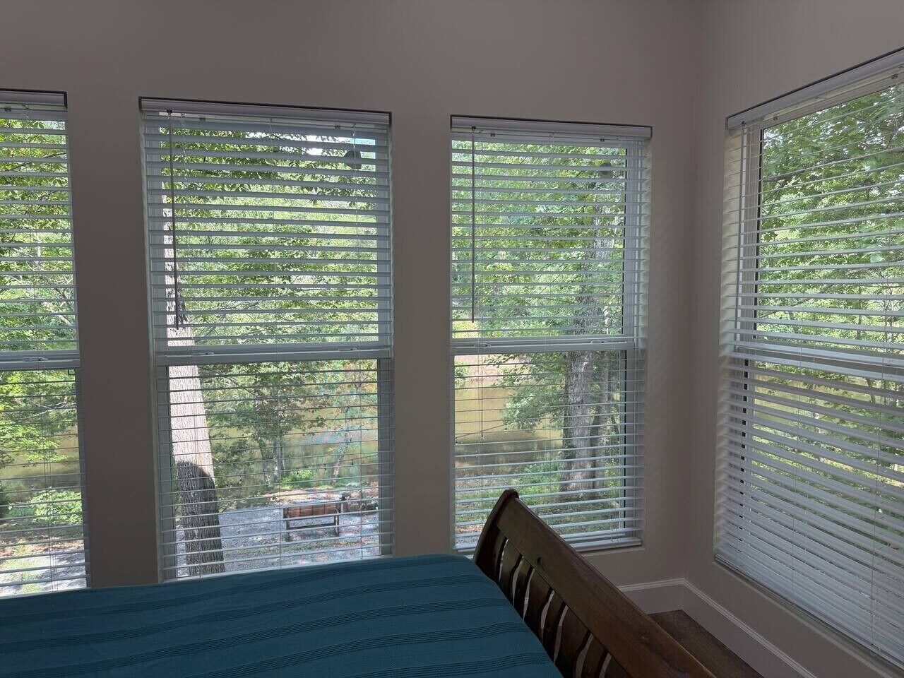 A bedroom with a bed, three windows, and a view of trees and a fence.
