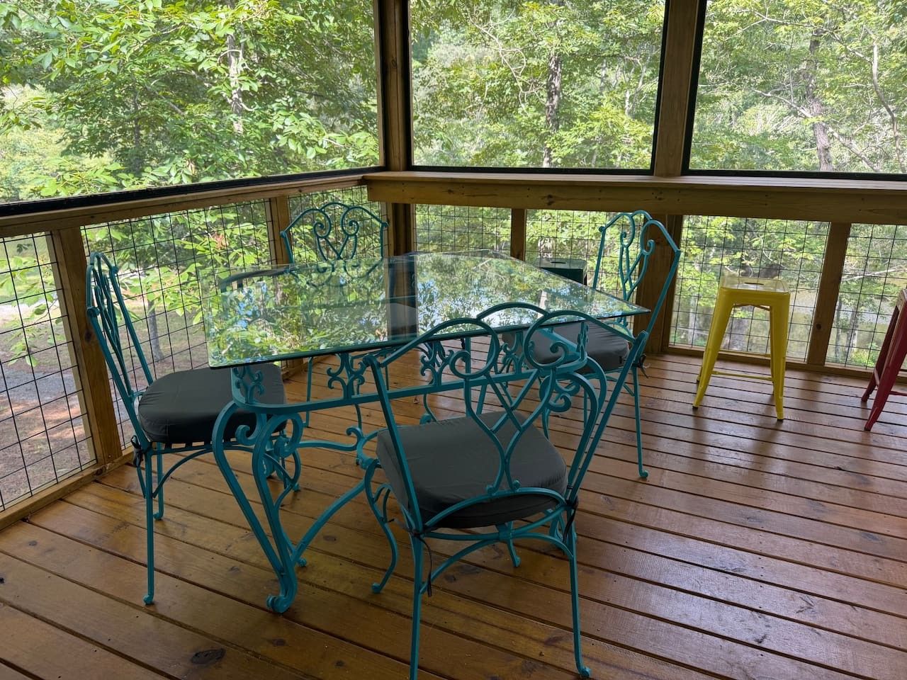 Un espace extérieur abrité, doté d’une table en verre et de chaises en métal, entouré d’une terrasse en bois et d’une rambarde en métal.