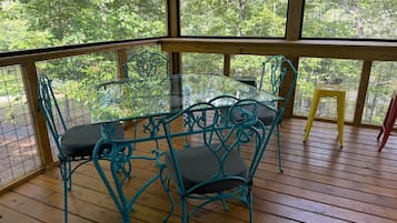 Un espace extérieur abrité, doté d’une table en verre et de chaises en métal, entouré d’une terrasse en bois et d’une rambarde en métal.