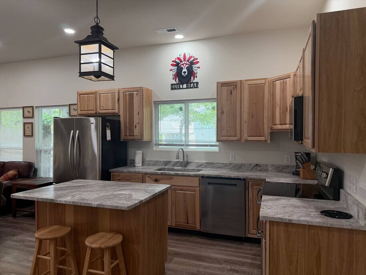 A modern kitchen with wooden cabinets, a stainless steel refrigerator, a sink, and a large island with stools.